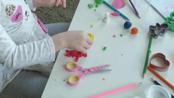 Šťastná holčička si hraje s plastelínou, modeluje postavu, na ploše jsou postavy a barevné tužky, rozvoj jemné motoriky rukou — Stock video