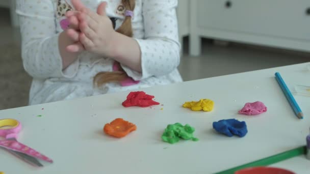 Feliz niña juega con plastilina de colores, esculpe una figura, en el escritorio son figuras y lápices de colores, el desarrollo de habilidades motoras finas de las manos — Vídeos de Stock