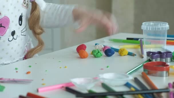 Menina feliz brinca com plasticina colorida, bolas de rolos, mãos na área de trabalho são figuras e lápis de cor, o desenvolvimento de habilidades motoras finas de mãos — Vídeo de Stock