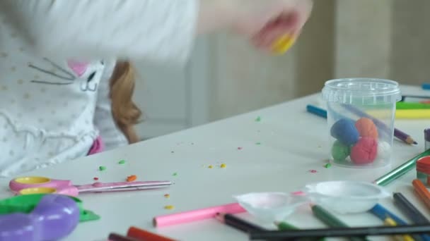 Uma menina pequena feliz tira a plasticina multicolorida de um recipiente, na área de trabalho são figuras e lápis coloridos, o desenvolvimento de habilidades motoras finas de mãos — Vídeo de Stock