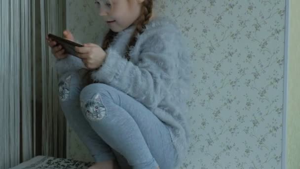 Niña Feliz Con Coletas Utiliza Teléfono Juega Sonriendo Sentado Habitación — Vídeo de stock