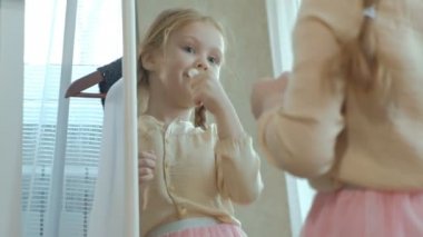 pigtails pembe bir etek ile neşeli küçük kız dudaklarına ruj ayna, ona anne gardırop önünde boyalar