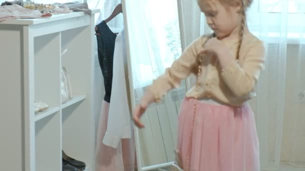 Fröhliches kleines Mädchen mit Zöpfen im rosafarbenen Rock probiert die Schuhe der Mutter auf Absätzen an und tanzt vor einem Spiegel mit einer Tasche, dem Kleiderschrank der Mutter — Stockvideo