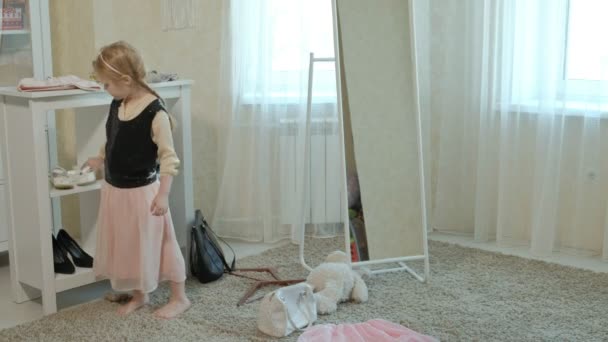 Cheerful girl with pigtails in a pink skirt tries on adult mothers clothes, dresses, high heels and dances in front of a mirror with a bag, mothers wardrobe — Stock Video