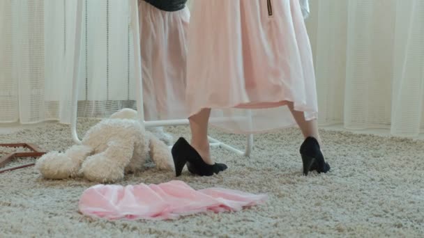 Χαρούμενο κορίτσι με κοτσίδες που προσπαθούν για ρούχα ενηλίκων μητέρες, φορέματα, ψηλά τακούνια και χορούς μπροστά από έναν καθρέφτη με μια τσάντα, μητέρες ντουλάπα, γκρο πλαν των ποδιών — Αρχείο Βίντεο
