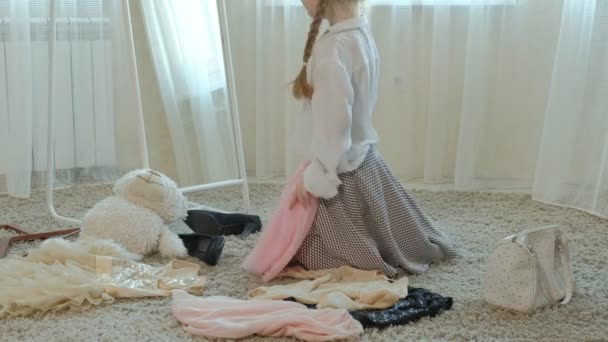 Vrolijk meisje met pigtails in een roze rok probeert op volwassen moeders kleding, jurken, hoge hakken en dansen voor een spiegel met een zak, moeders kledingkast — Stockvideo