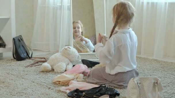 Vrolijk meisje met pigtails in een roze rok probeert op volwassen moeders kleding, jurken, hoge hakken en dansen voor een spiegel met een zak, moeders kledingkast — Stockvideo