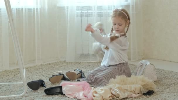 Chica alegre con coletas en una falda rosa se prueba la ropa de madres adultas, vestidos, tacones altos y bailes delante de un espejo con una bolsa, armario de las madres — Vídeo de stock