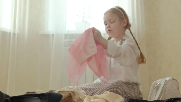Menina alegre com tranças em uma saia rosa tenta em mães adultas roupas, vestidos, saltos altos e danças na frente de um espelho com uma bolsa, guarda-roupa mães — Vídeo de Stock