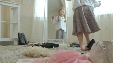 Yetişkin anneler elbise, elbise, topuklu ve dansları bir çanta, anneler gardırop bir ayna önünde neşeli kız pigtails pembe bir etek ile çalışır