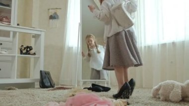 Yetişkin anneler elbise, elbise, topuklu ve dansları bir çanta, anneler gardırop bir ayna önünde neşeli kız pigtails pembe bir etek ile çalışır