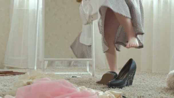 Glad flicka med flätor i en rosa kjol försöker på vuxen mödrar kläder, klänningar, höga klackar och danser framför en spegel med en väska, mödrar garderob — Stockvideo