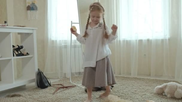 Χαρούμενο κορίτσι με κοτσίδες με ένα ροζ φούστα προσπαθεί ενηλίκων μητέρες ρούχα, φορέματα, ψηλά τακούνια και χορούς μπροστά από έναν καθρέφτη με μια τσάντα, μητέρες ντουλάπα — Αρχείο Βίντεο