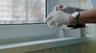 Lastik eldiven bir erkekte bir pencere pervazına geri yükler, Yapıştır hasarlı bölgeleri için bir spatula ile geçerlidir.