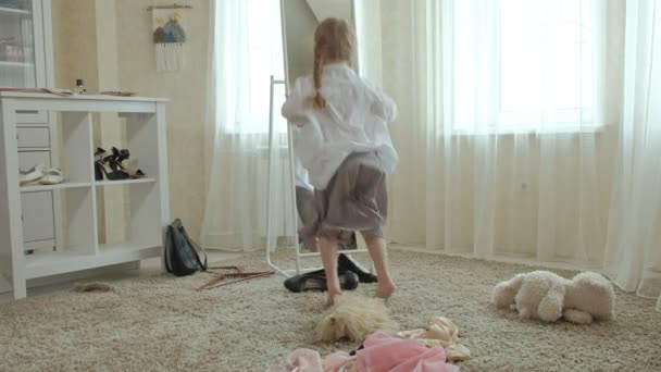 Fille gaie avec des queues de cochon dans une jupe rose essaie sur les vêtements des mères adultes, robes, talons hauts et danses devant un miroir avec un sac, garde-robe des mères — Video