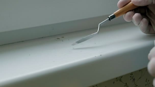 Um homem com luvas de borracha restaura um peitoril da janela, aplica colar em áreas danificadas com uma espátula — Vídeo de Stock