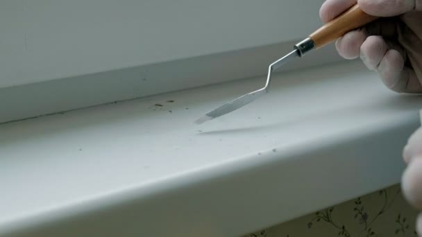 Un hombre con guantes de goma restaura un alféizar de la ventana, aplica pasta a las zonas dañadas con una espátula — Vídeos de Stock