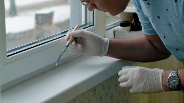 Un hombre con guantes de goma restaura un alféizar de la ventana, aplica pasta a las zonas dañadas con una espátula — Vídeos de Stock