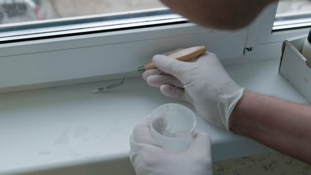 Un hombre con guantes de goma restaura un alféizar de la ventana, aplica pasta a las zonas dañadas con una espátula — Vídeos de Stock