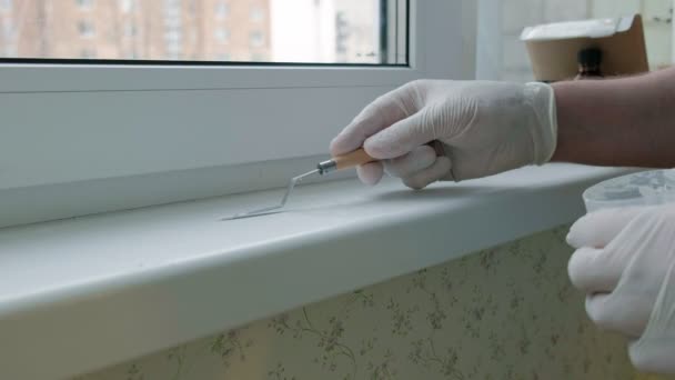 Un hombre con guantes de goma restaura un alféizar de la ventana, aplica pasta a las zonas dañadas con una espátula — Vídeos de Stock