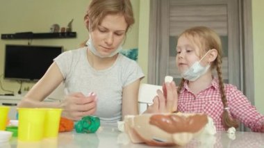 Genç bir kadın ve bir kız dişlerini gelen hamuru kalıp, dişlerini bir oyuncak çene içine yerleştirin, diş hekimi, anne ve kızı oynamak