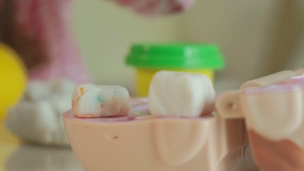 Una mujer joven y una niña moldean sus dientes de plastilina, una niña inserta sus dientes en la mandíbula encarnada, juega en el dentista, madre e hija, primer plano de la mano — Vídeo de stock