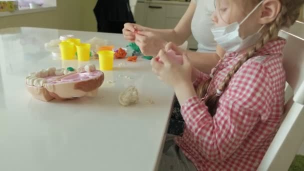 Молодая женщина и девушка вылепляют зубы из пластилина, вставляют зубы в игрушечную челюсть, играют стоматолога, мать и дочь — стоковое видео