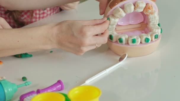 En ung kvinna och en flicka forma sina tänder från Plastilina sätt tänderna i en leksak käke, ange hängslen, spela en tandläkare, mor och dotter — Stockvideo