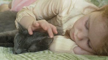 mutlu kız çocuğu sarı saçları ve pigtails bir gri kedi konturlama kanepede yatan ile