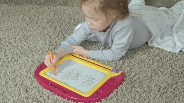 Dziewczynka z rude włosy faliste leży na podłodze i rysuje na tablicy magnetycznej. Pojęcie procesu edukacji. — Wideo stockowe