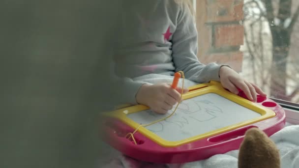 Kırmızı dalgalı saçlı küçük bir kız yerde yatıyor ve manyetik bir tahtaya çizer. Eğitim sürecinde kavramı. yakın çekim — Stok video