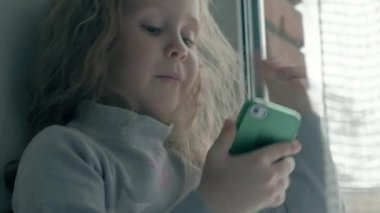 pencere kenarında otururken, bir battaniye kapsayan ve telefonla konuşurken, dalgalı Kızıl saçlı video arama, yakın çekim portre mutlu küçük kız