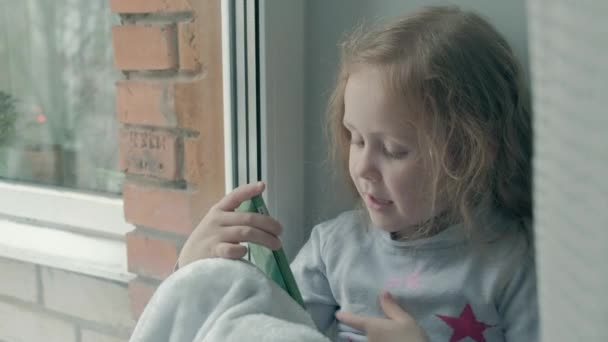 Bambina felice con i capelli rossi ondulati seduta sul davanzale della finestra, coprendo una coperta e usando il telefono, parlando, videochiamata, ritratto ravvicinato — Video Stock