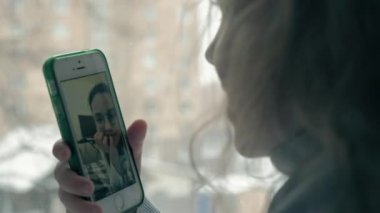pencere kenarında otururken, bir battaniye kapsayan ve telefonla konuşurken, dalgalı Kızıl saçlı video arama, yakın çekim portre mutlu küçük kız