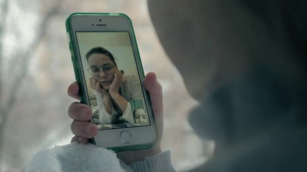 Heureuse petite fille aux cheveux roux ondulés assise sur le rebord de la fenêtre, couvrant une couverture et utilisant le téléphone, parlant, appel vidéo, portrait en gros plan — Video