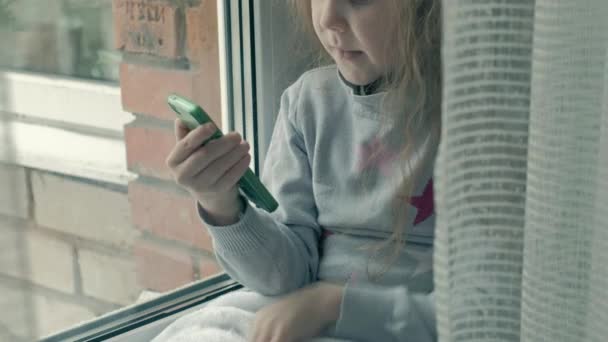 Niña feliz con el pelo rojo ondulado sentado en el alféizar de la ventana, cubriendo una manta y utilizando el teléfono, hablando, videollamadas, primer plano retrato — Vídeos de Stock