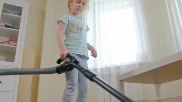 A little girl with blond hair cleans up with a vacuum cleaner, brings order and cleanliness, helps mom — Stock Video