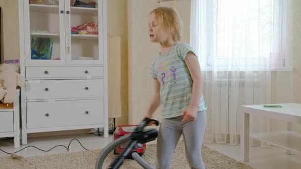 A little girl with blond hair cleans up with a vacuum cleaner, brings order and cleanliness, helps mom — Stock Video