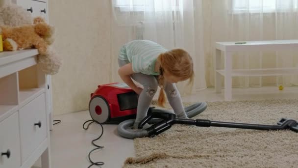 A little girl with blond hair sits on a vacuum cleaner and cleans up, brings order and cleanliness, helps mom — Stock Video