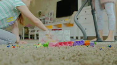 Anne ve kızı, bir vakum cleaner, sarı saçlı toplar oyuncaklar, tasarımcı bir kap içinde yardımcı olur anne, küçük bir kızla yakın çekim ile genç bir kadın temizler