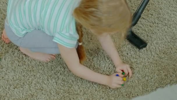 Mom and daughter, a young woman cleans up with a vacuum cleaner, a little girl with blond hair collects toys, the designer in a container, helps mom — Stock Video