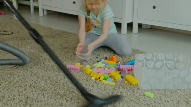 Мама и дочь, молодая женщина убирает пылесосом, маленькая девочка с светлыми волосами собирает игрушки, дизайнер в контейнере, помогает маме — стоковое видео