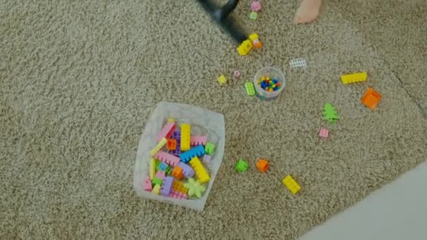 Maman et sa fille, une jeune femme nettoie avec un aspirateur, une petite fille aux cheveux blonds collecte des jouets, le designer dans un récipient, aide maman — Video