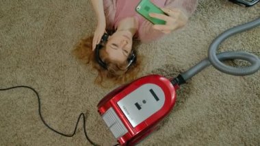 mutlu genç kadın ya da yarı-kulaklıklar, yalan ev hanımı bir elektrikli süpürge ile telefon kullanır, müzik, dans, Temizleme, kat hizmetleri, en iyi görünüm için dinler