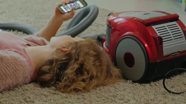 Happy young woman or a housewife with a vacuum cleaner, lying on the floor, using the phone, having fun, playing, cleaning, household — Stock Video