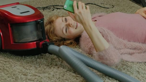 Šťastná mladá žena v domácnosti s vysavačem, ležící na podlaze, pomocí telefonu, baví, přehrávání nebo úklid, domácí — Stock video