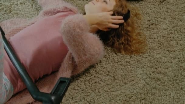 Happy young woman or housewife with a vacuum cleaner, lying on the half-headphones, uses the phone, listens to music, dances, cleaning, housekeeping, top view — Stock Video
