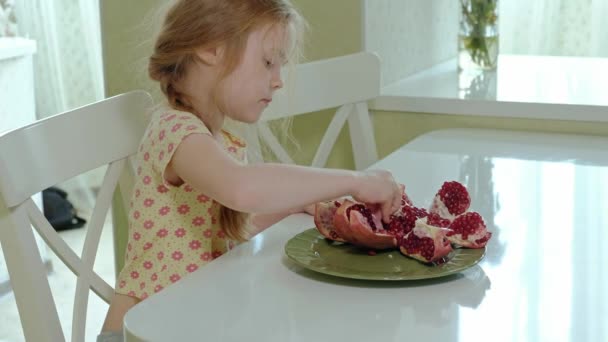 Счастливая маленькая девочка с светлыми волосами ест гранат, концепция здоровой пищи, портрет крупным планом — стоковое видео