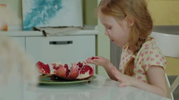 Щаслива маленька дівчинка з світлим волоссям їсть гранат, концепція здорової їжі, портрет крупним планом — стокове відео