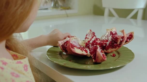 Happy little girl with blond hair eats pomegranate, healthy food concept, close-up — Stock Video